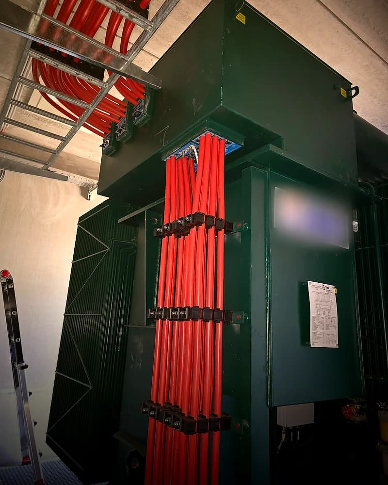 Groene transformator met rode kabels in kabelklemmen.