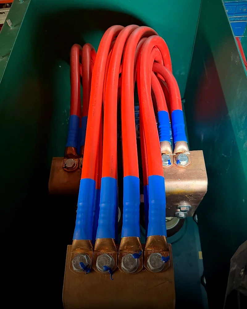 Rode kabels met blauwe krimpkous op een messing rail in een groene kast.
